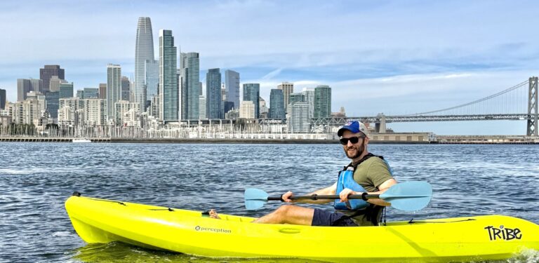 A paddler in a yellow sit-on-top kayak with the whole downtown skyline behind.