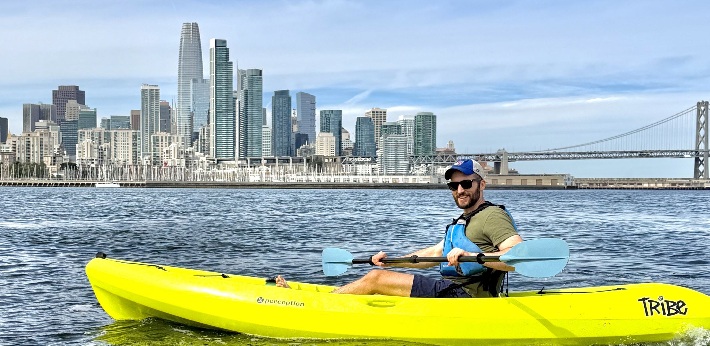 A paddler in a yellow sit-on-top kayak with the whole downtown skyline behind.