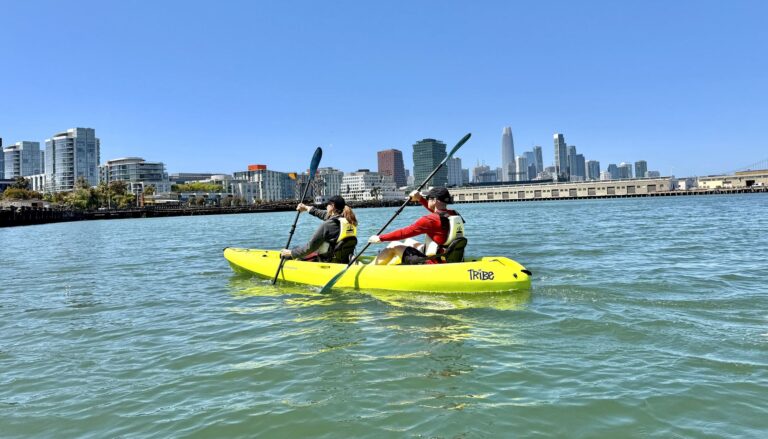 A single kayaker on flat water with the city behind.