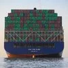 A container ship seen bow-on, its deck stacked with green and red containers.