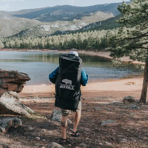 A paddler carrying an inflatable board in a backpack down to a mountain lake.
