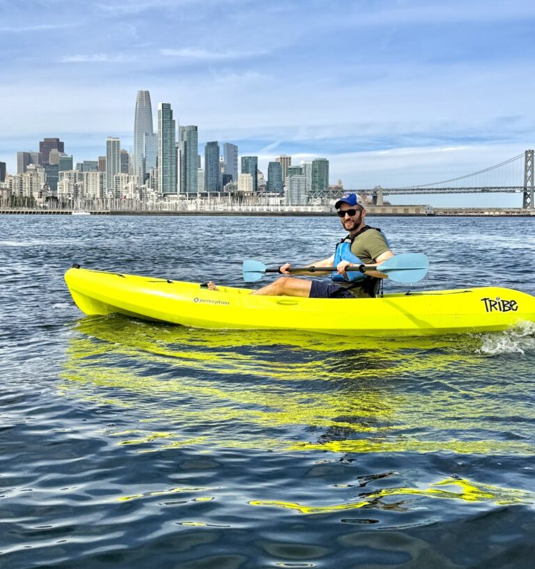 A solo kayaker on open water with the city skyline behind.