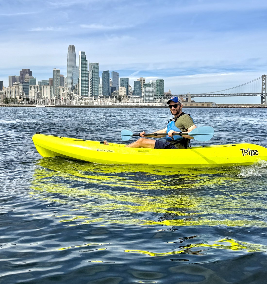 A solo kayaker on open water with the city skyline behind.