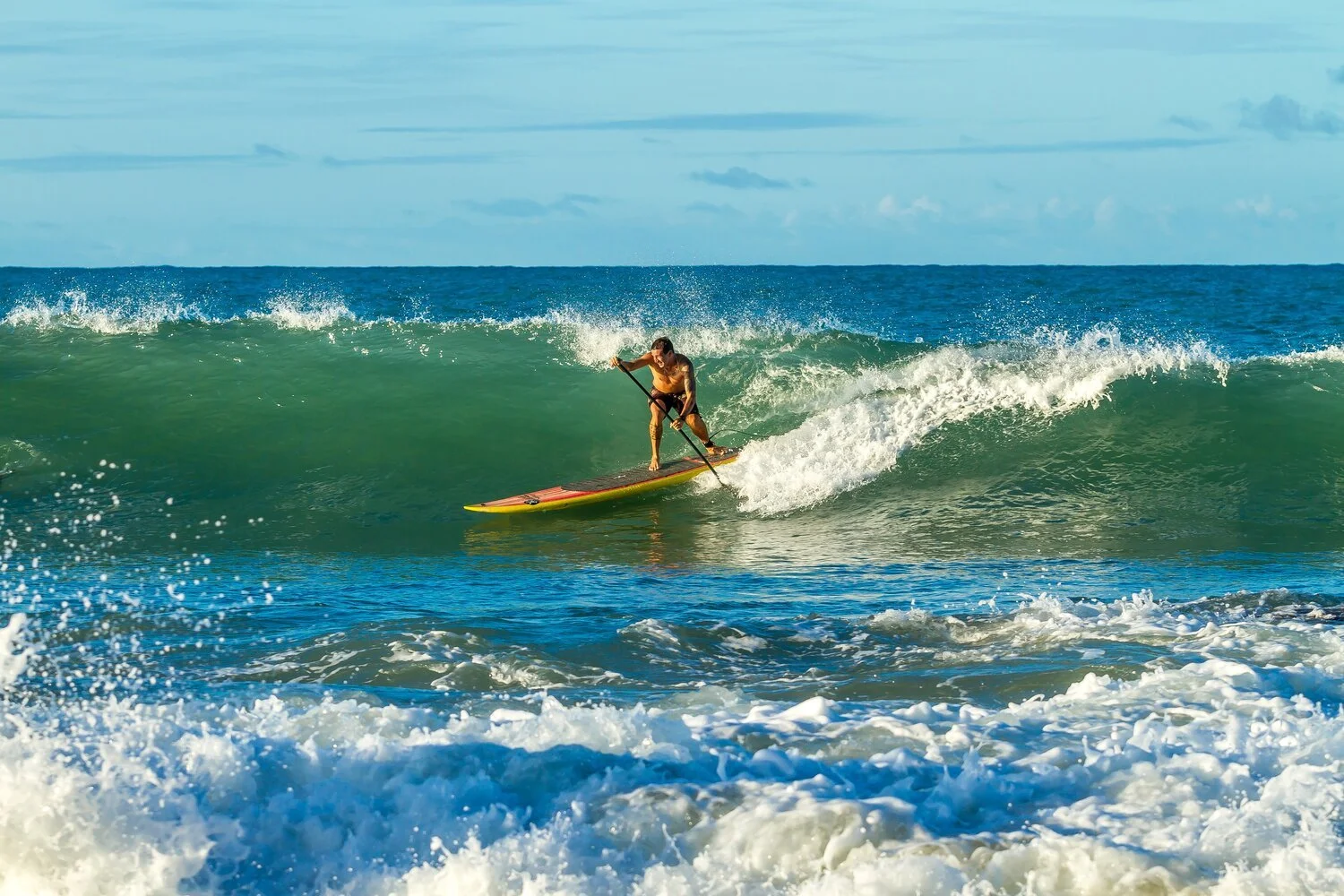 A paddler riding a longboard SUP across the face of a breaking wave.