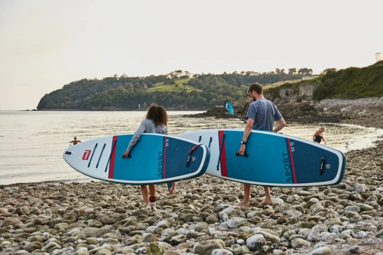 Two inflatable paddleboards standing upright on a pebble beach.