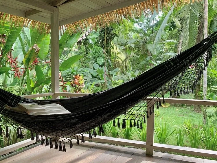 A black hammock on a deck overlooking dense jungle.