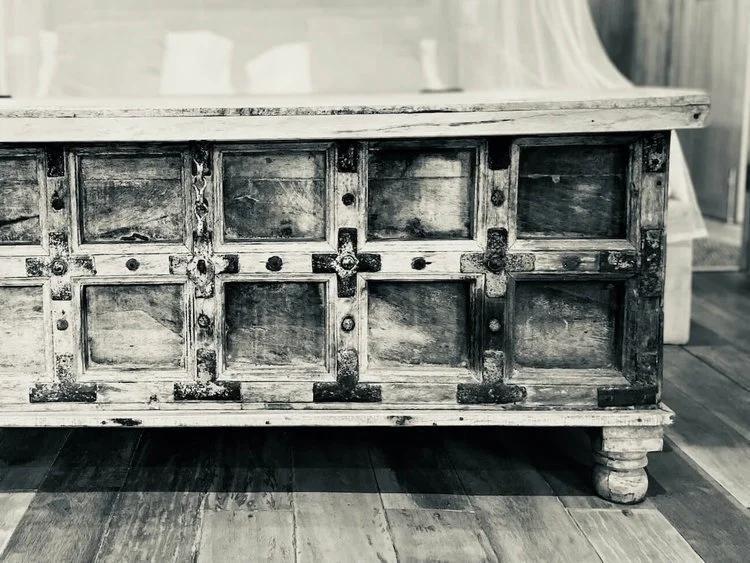 A carved wooden chest standing against a plank wall, in black and white.