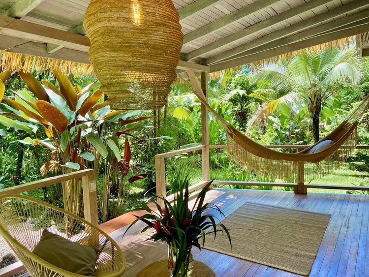 A hammock strung across a covered deck among tropical planting.