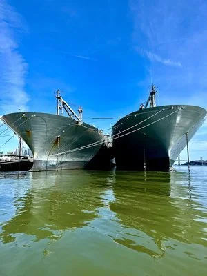 The bows of two moored ships side by side above green water.