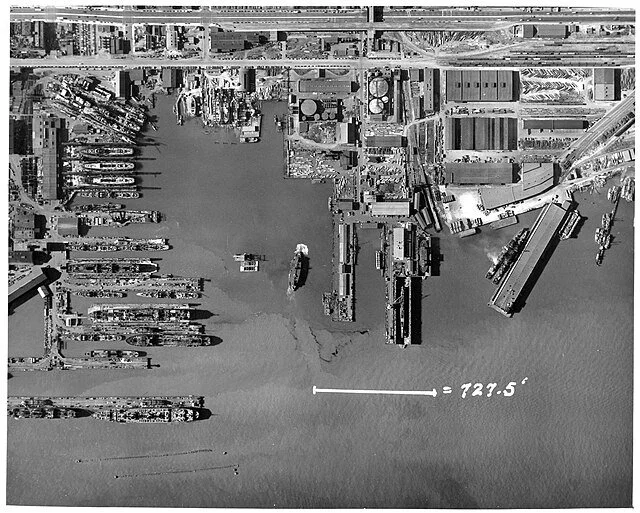 An aerial survey photograph of the shipyard with a 727.5 foot dimension marked across the water.