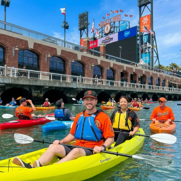 Two paddlers in a yellow kayak in front of the brick wall of Oracle Park.