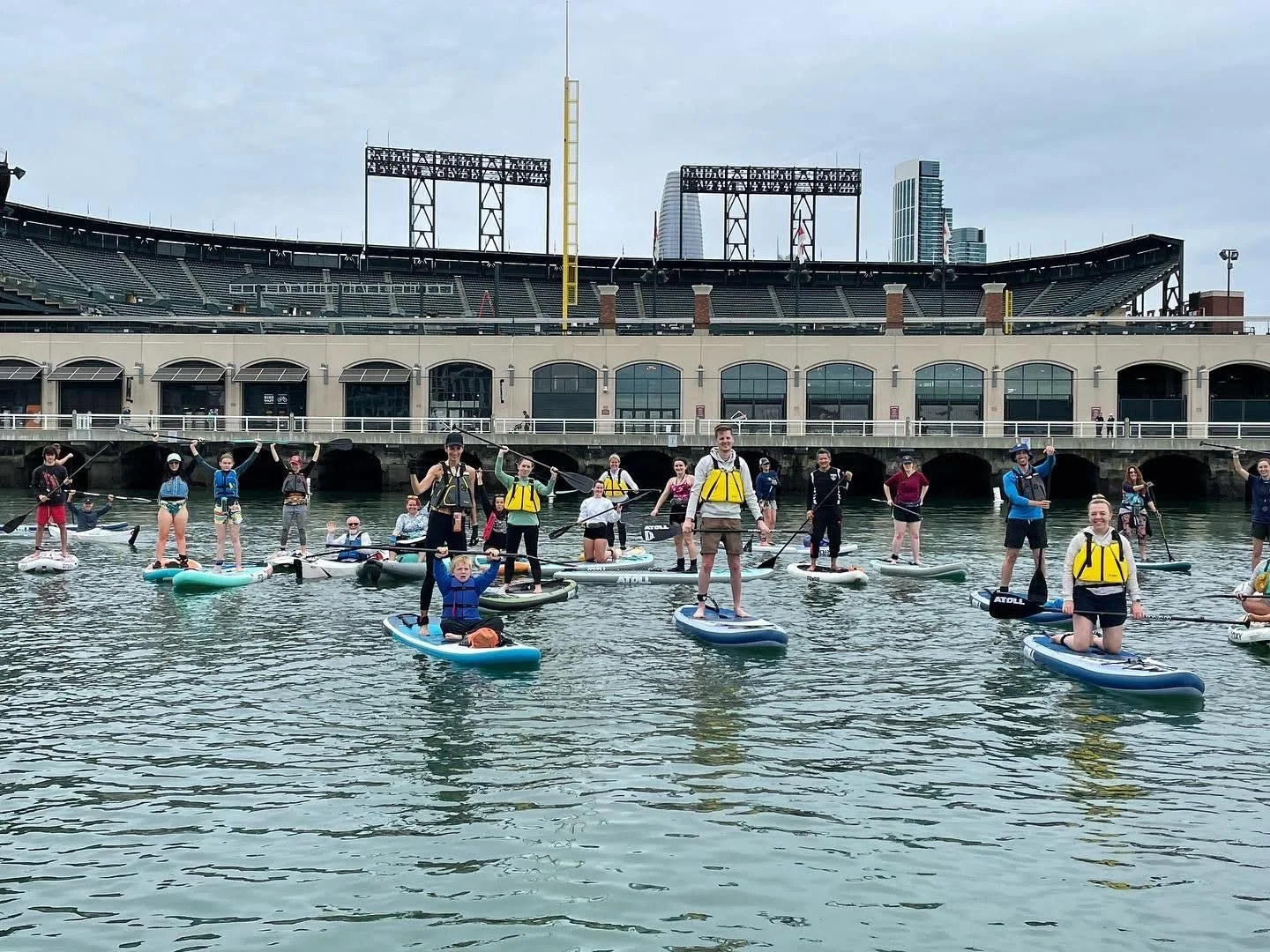 A line of paddlers on the water in front of Oracle Park.