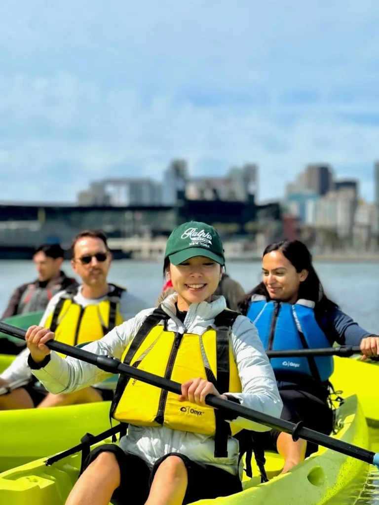 Four people in two yellow kayaks with the city skyline behind them.