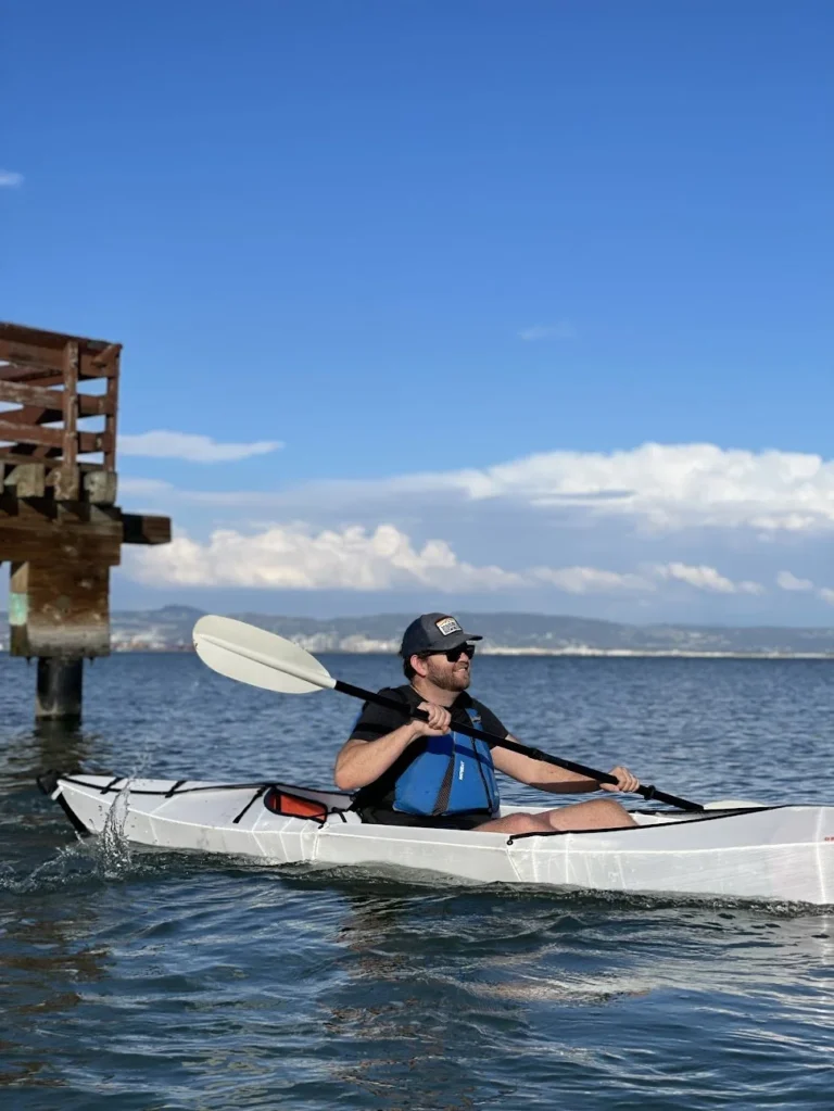 A kayaker in a white sea kayak on flat water.