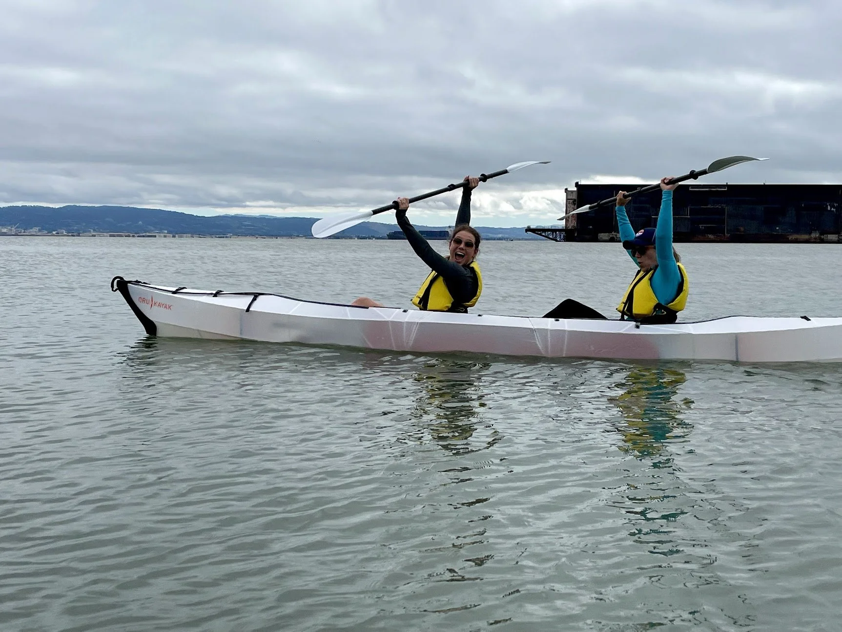 Two people in a white sea kayak holding their paddles above their heads.