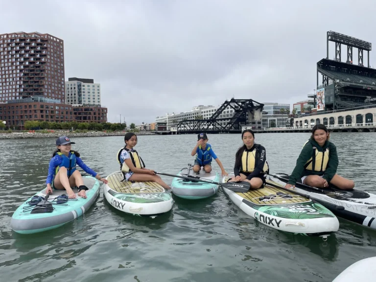 Paddlers on boards and kayaks in front of the brick wall of Oracle Park.