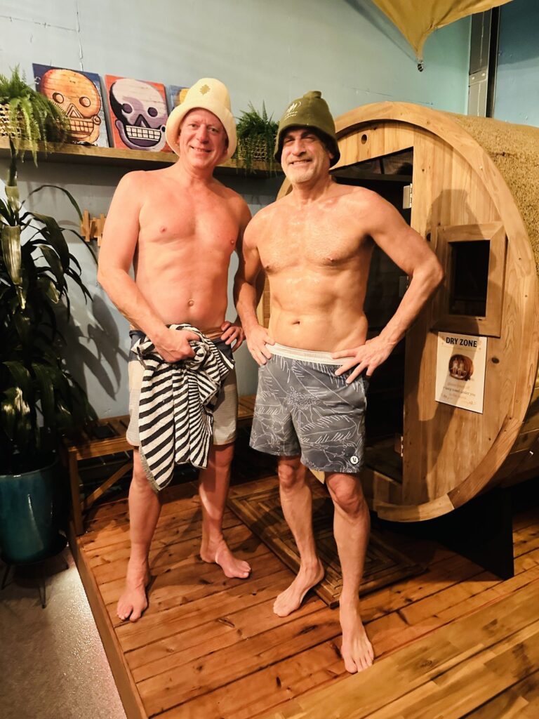 Two people standing in front of the barrel sauna after a session.