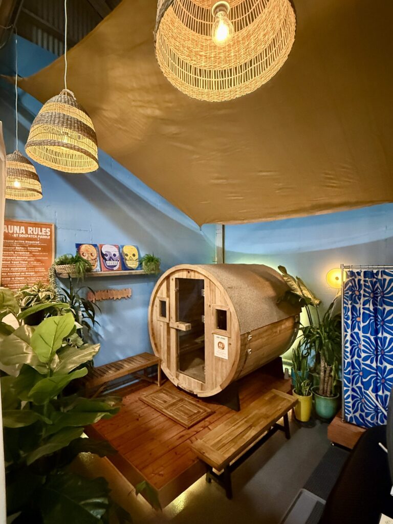 The barrel sauna in the room at Crane Cove, plants around it and a bench in front.