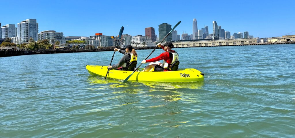 A kayaker on bright water with the downtown San Francisco skyline behind.