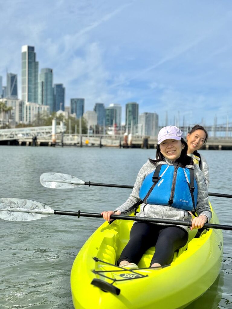 Two paddlers in a tandem kayak with the city skyline behind them.